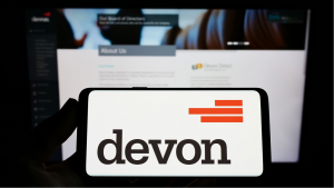 컴퓨터 화면 앞에 Devon Energy Corporation 로고가 표시된 스마트폰을 들고 있는 손 이미지