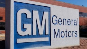 배경에 파란색과 흰색 로고 및 벽돌 건물이 있는 General Motors(GM) 기호