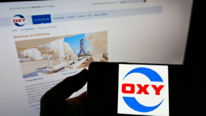 웹사이트 앞 화면에 미국 회사 Occidental Petroleum Corp.(OXY)의 로고가 있는 휴대폰을 들고 있는 사람. 전화 디스플레이에 중점을 둡니다. 수정되지 않은 사진.